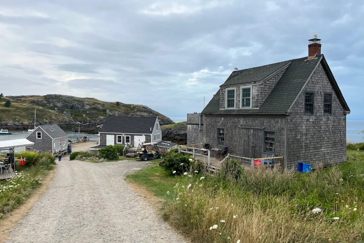 Weathered shingled cottage beside a gravel lane near the water