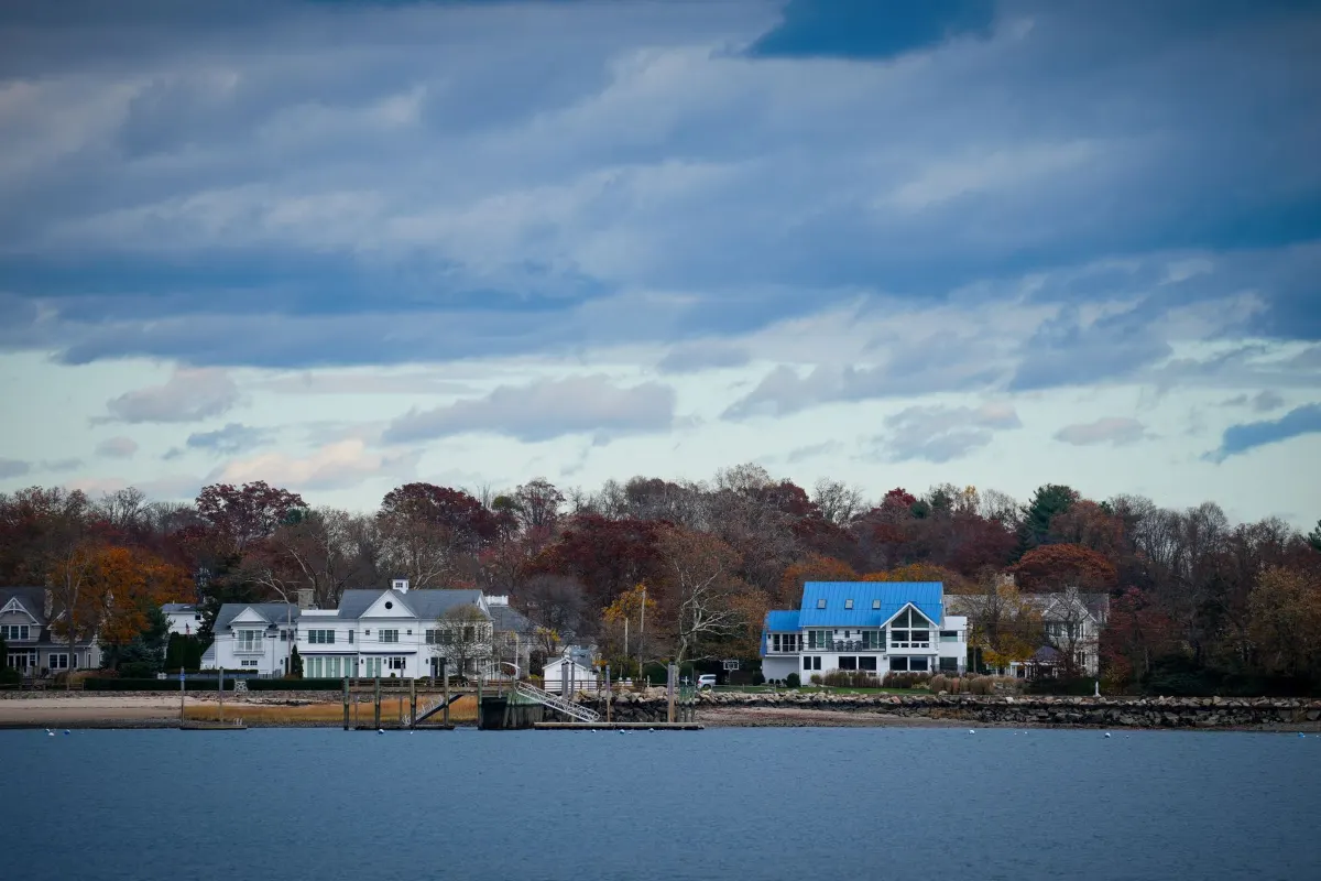 Houses along a shoreline with autumn trees under a cloudy sky